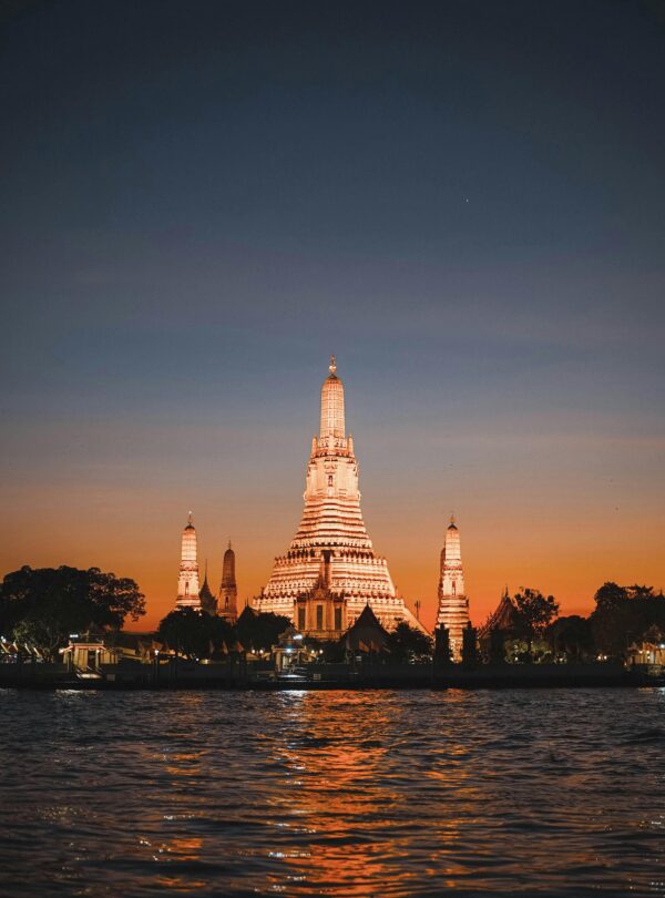 Beautiful view of Wat Arun temple illuminated during sunset along the Chao Phraya River in Bangkok, Thailand.