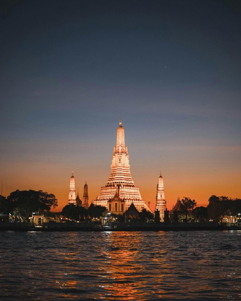 Beautiful view of Wat Arun temple illuminated during sunset along the Chao Phraya River in Bangkok, Thailand.