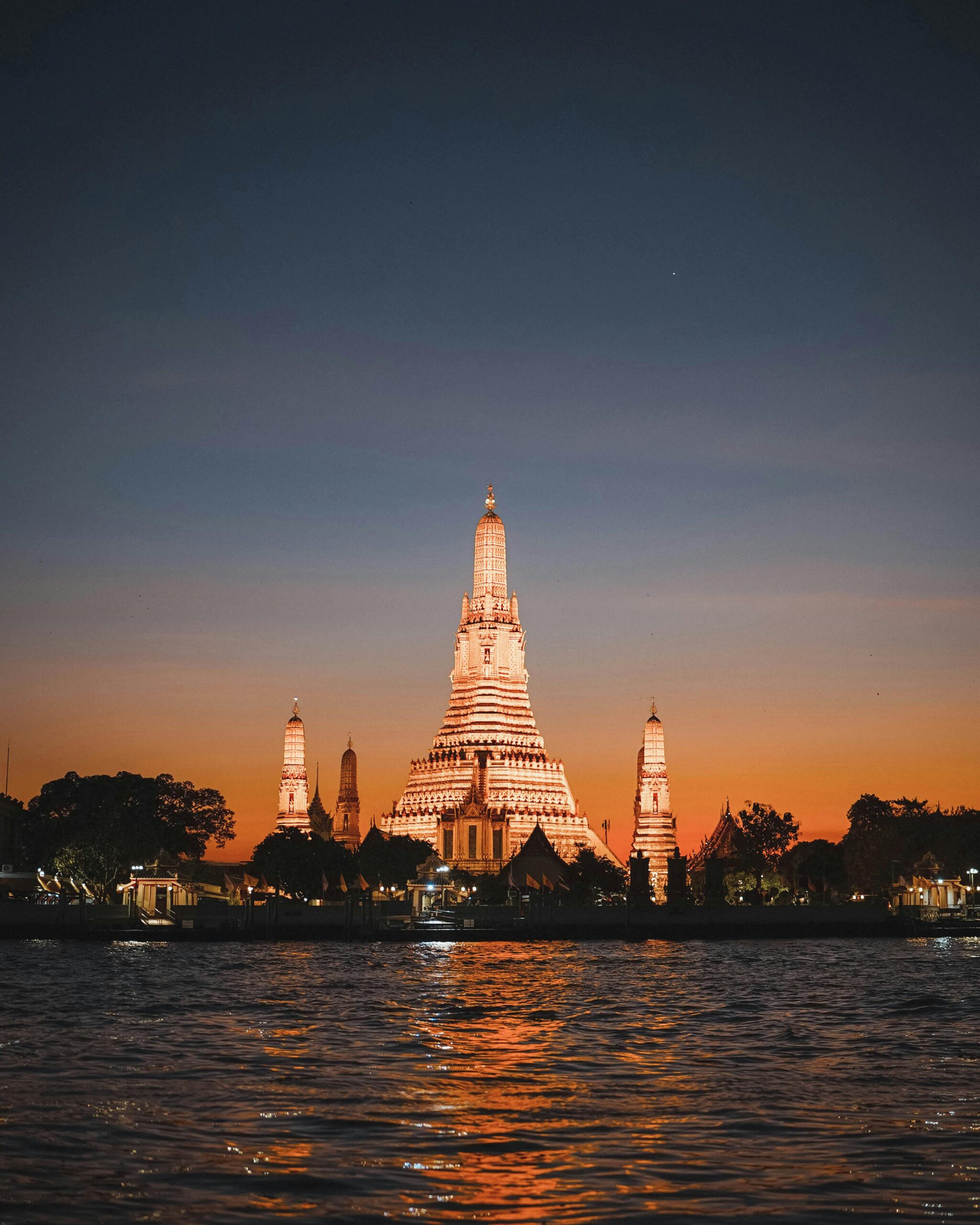 Beautiful view of Wat Arun temple illuminated during sunset along the Chao Phraya River in Bangkok, Thailand.